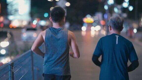 后视图亚洲华人活跃的老人和儿子晚上下班后一起在城里跑步慢跑