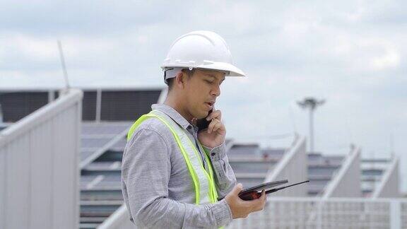 电气工程师在屋顶上检查太阳能电池板的构造并使用智能手机和数码平板电脑