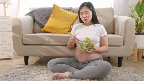 快乐的亚洲孕妇在家里的沙发上吃沙拉怀孕期间吃很多不同的蔬菜健康的怀孕观念