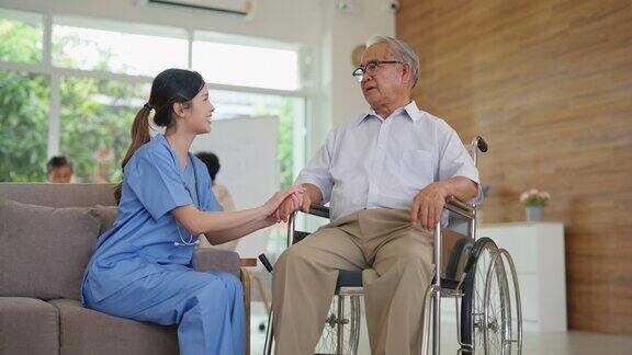 年轻的亚洲护理医生坐在老人院客厅轮椅上的老人旁边精神保健和健康护士带着微笑照顾老人和理疗