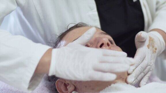 在美容诊所接受补水手术的女性客户在油性痤疮皮肤上涂抹保湿霜的特写