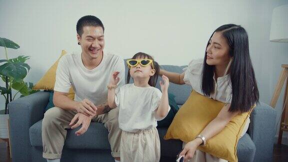 年轻的亚洲家庭父母带着他们的孩子戴着太阳镜坐在沙发上玩在一起在家里的客厅里