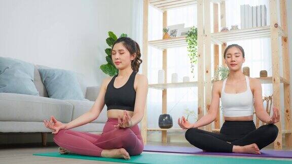 亚洲女性朋友一起在家做瑜伽普拉提迷人的女孩穿着运动服用垫子在家里的客厅里度过自由的休闲时光进行保健运动