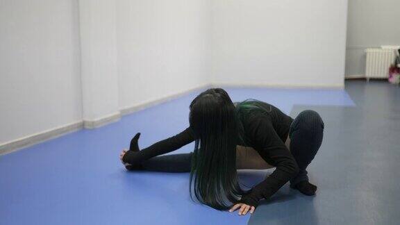 一名绿色头发的年轻亚洲女子穿着瑜伽裤和运动服在健身房里热身