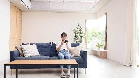 一个亚洲女人在沙发上玩智能手机