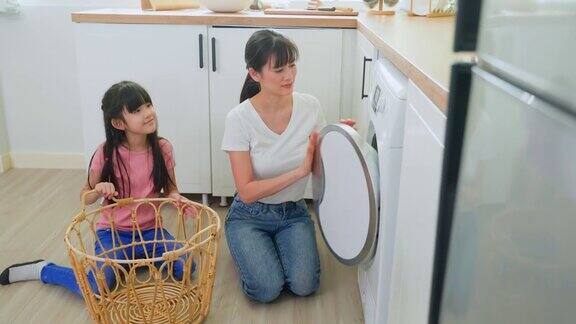 亚喜一家人待在家里妈妈教女儿洗脏衣服年幼可爱的小女孩帮助父母妈妈把衣服放在家里的洗衣机里Domestic-Housekeeping