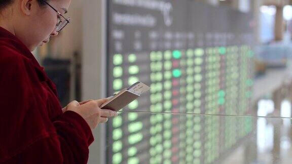亚洲旅行者女性使用智能手机在机场等待登机时查看航班信息屏幕