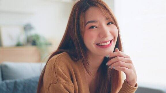 自信微笑年轻的亚洲女性看着相机坐在家里快乐美丽的女士漂亮的脸牙齿微笑独自在室内摆姿势