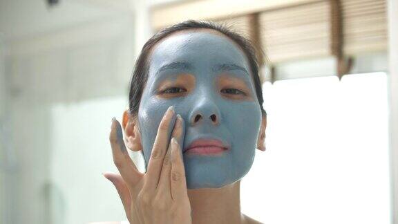亚洲人戴着蓝色保湿面膜在家浴室里看着镜头