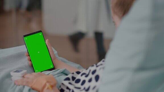 生病的女孩拿着模拟绿屏色度键手机与隔离显示期间恢复