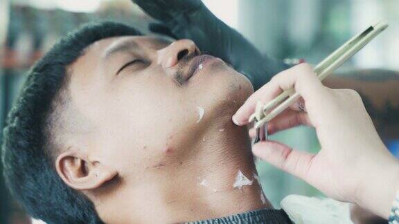 一名亚洲男子在理发店用电动剃须刀和剃刀剪头发和留胡子