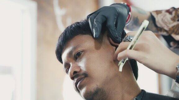 一名亚洲男子在理发店用电动剃须刀和剃刀剪头发和留胡子