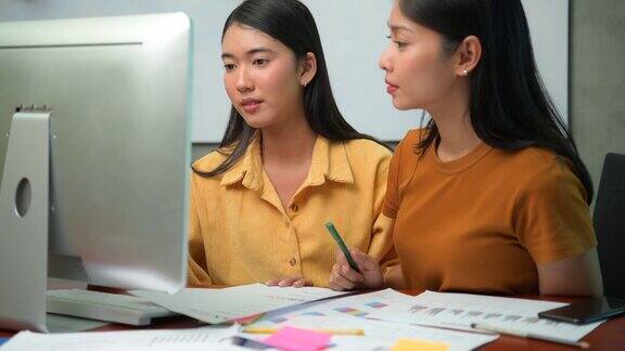 两个亚洲商务办公室的妇女讨论想法而工作与台式电脑在办公室