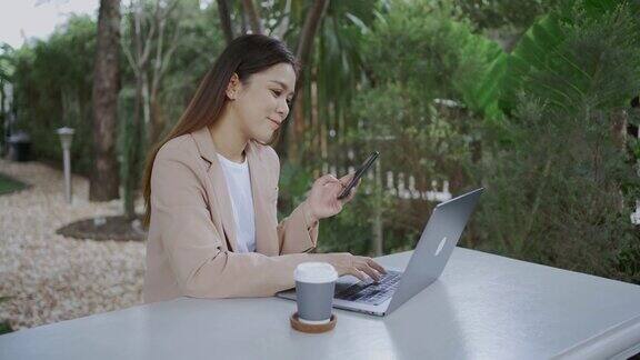 快乐的女商人一边在咖啡馆工作一边使用手机和笔记本电脑