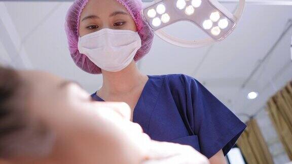从顾客的低角度看人脸一名女医生戴着卫生手套戴着手术帽在手术光下检查面部皮肤然后注射肉毒杆菌维生素C在眼部部位穿着浴袍躺在白色的医疗沙发上