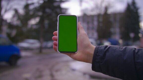 手握手机的人使用一个垂直的绿色屏幕背景上的街道房屋关键智能手机技术触摸信息显示