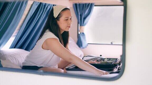 窗外景色:亚洲中部妇女在休闲布坐在床上在露营车整理她的行李感觉快乐和放松的假期独自旅行