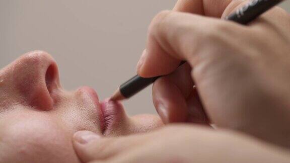 专业美容师在唇妆前用铅笔画唇线Cosmetological过程美丽孤立背景模糊