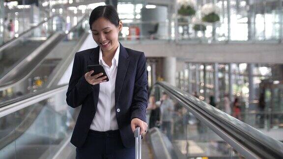 亚洲女商人在机场候机楼的自动扶梯上使用电话