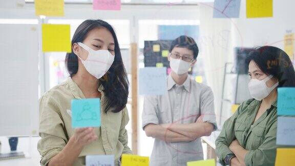 亚洲年轻的商人们讨论商业头脑风暴会议一起分享数据带着医用口罩在办公室里写玻璃墙