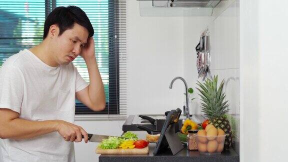 一名压力大的男子在家里的厨房里用平板电脑按照菜谱烹饪蔬菜