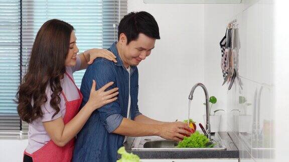 年轻夫妇在家里厨房的水槽里洗蔬菜女人给男人按摩