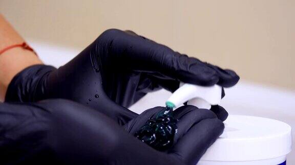 特写双手在黑色医疗手套挤出化妆品绿色凝胶从一个分配器医学、美容防腐剂