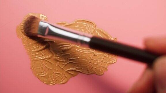 在粉红色背景上涂抹粉底色调棕色奶油纹理特写使用笔刷化妆品和美容产品概念化妆品眼影调色板古铜色或遮瑕