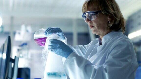 安全眼镜高级女化学家在烧杯中混合吸烟液体她在一家明亮的现代实验室工作