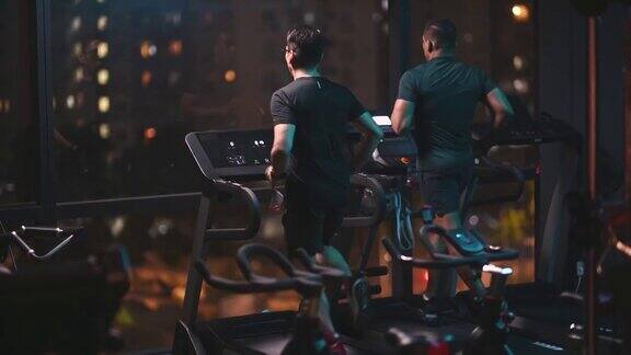 后视图身体强壮的男人一起在健身房跑步机在晚上面对城市街灯