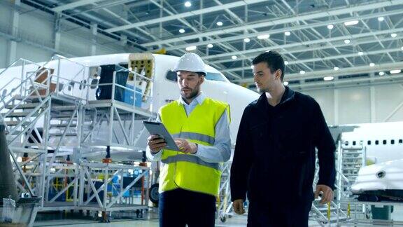飞机维修机械师和总工程师使用数字平板电脑走过大飞机开发设施他们分析、检查、开发和设计飞机