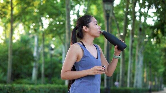 亚洲健身年轻女子在公园跑步后喝水