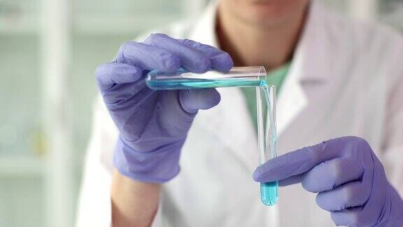 戴着手套的科学家在实验室将蓝色透明液体倒入试管