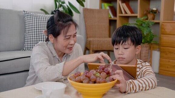 4K亚洲单身妈妈正试图教她的小儿子做作业同时奖励他葡萄一个亚洲男孩坐在客厅的房子中间教他的妈妈做作业