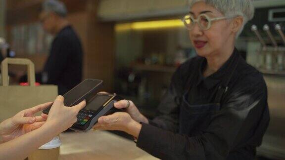 亚洲顾客在咖啡店购买咖啡后用手机扫描二维码支付