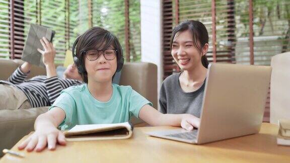 快乐的亚洲孩子男孩在线课程学习从家里亚洲孩子举手回答问题从在线老师亚洲男孩坐在父母从笔记本电脑学习在生活在家里