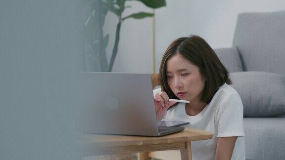 一位美丽的亚洲妇女在家用笔记本电脑工作