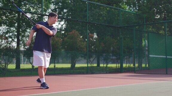 年轻的亚洲华裔唐氏综合症男子正在练习网球