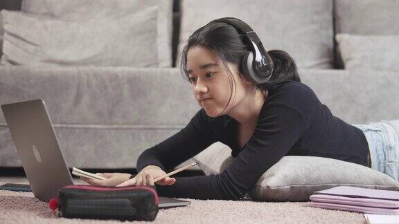 迷人的亚洲少女戴着耳机听和学习在平板电脑屏幕上与她的老师并在笔记本上写冠状病毒或冠状病毒19封锁情况视频电话技术与她的建议学习她的家庭作业