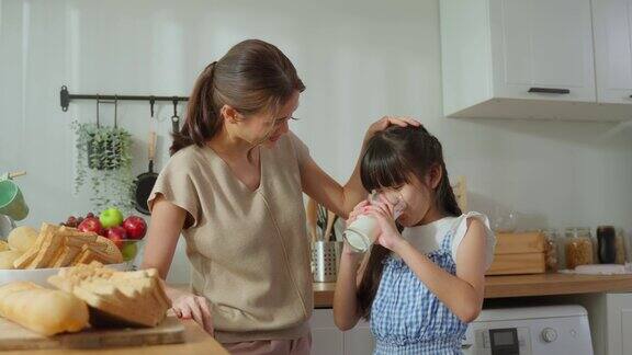 亚洲小可爱的孩子拿着一杯牛奶和喝妈妈迷人的妈妈教导和支持年轻的女儿照顾她的身体喝牛奶后醒来在家里的保健