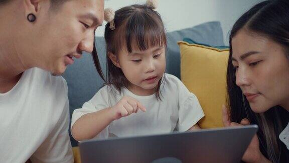 年轻的亚洲家庭坐在沙发上与孩子一起享受黄金时间的快乐时刻在家里的客厅里使用笔记本电脑看卡通电影