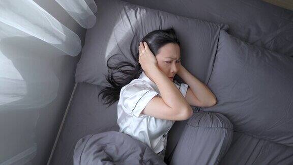 亚洲妇女因噪音问题而烦恼和不安试图盖着耳朵睡觉躺在床上前视图