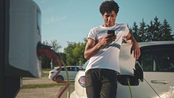 一名年轻男子在停车场充电时使用智能手机