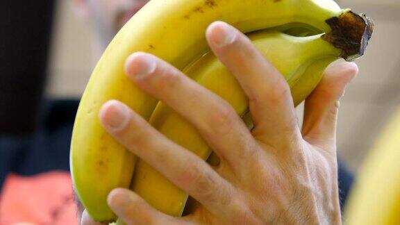 男手在超市挑选香蕉一个男人从杂货店的柜台上拿着一串香蕉小伙子正在商店的农产品部挑选新鲜水果买家选择食物近距离