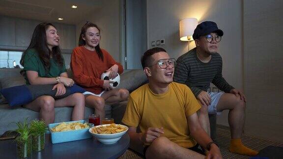 4K一群亚洲人朋友一起在电视上观看和欢呼比赛体育足球
