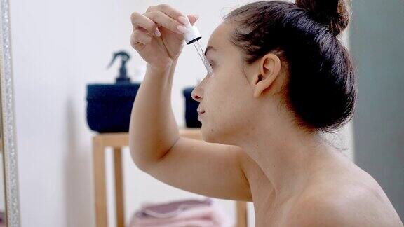 镜子时刻:女性抗衰老护肤在家中用精华液滴管涂抹玻尿酸