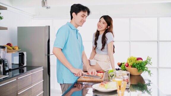 亚洲快乐的恩爱夫妻站在家里的厨房台子上愉快地交谈、准备和烹饪一起在自家厨房做饭两人4k实时视频