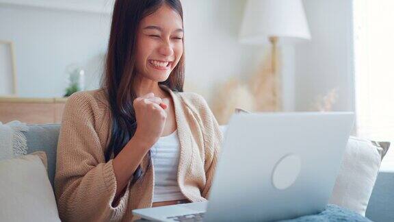 兴奋的年轻亚洲女冠军看着笔记本电脑庆祝在家办公成功惊喜在邮件中读到好消息完成目标项目