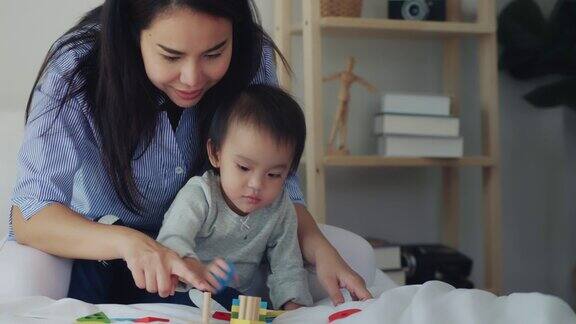 亚洲母亲和婴儿的孩子女孩学习玩彩色的木制玩具在床上