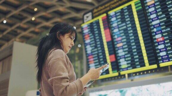亚洲女旅客在机场候机楼用智能手机查询航班时刻表